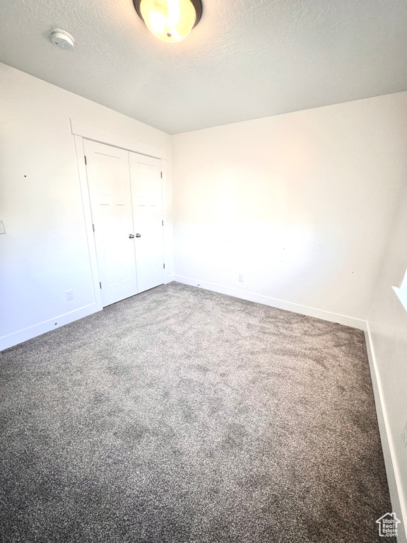 Unfurnished bedroom featuring a closet, a textured ceiling, and carpet flooring