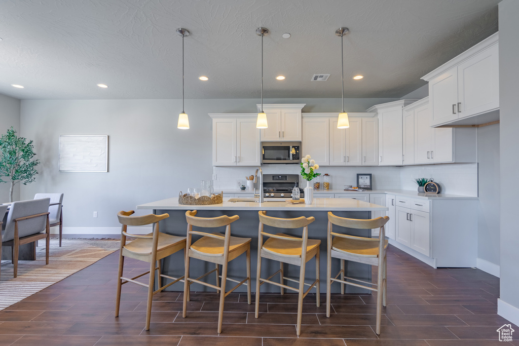 Kitchen featuring a kitchen island with sink, appliances with stainless steel finishes, dark hardwood / wood-style floors, and white cabinetry