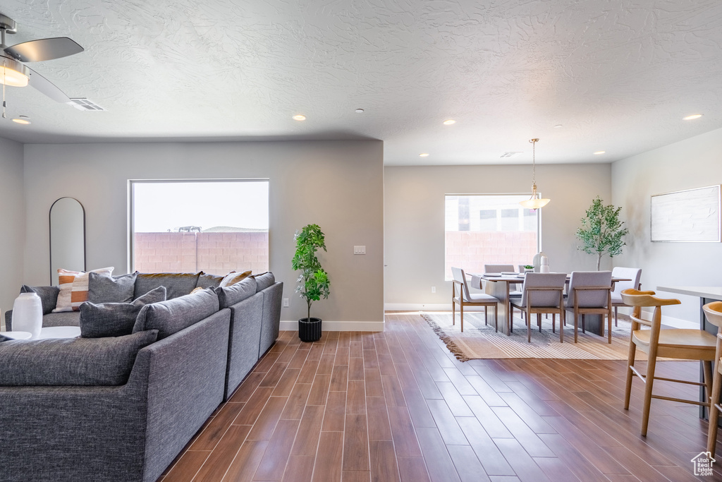Living room with ceiling fan, a textured ceiling, and dark wood-type flooring