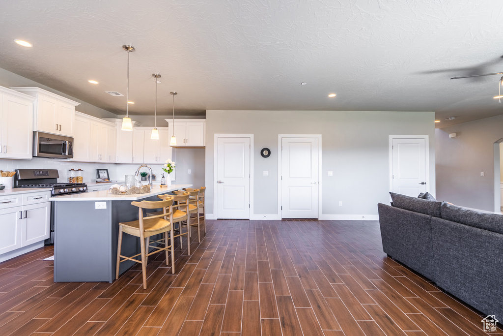 Kitchen featuring white cabinets, dark wood-type flooring, appliances with stainless steel finishes, and a kitchen island with sink