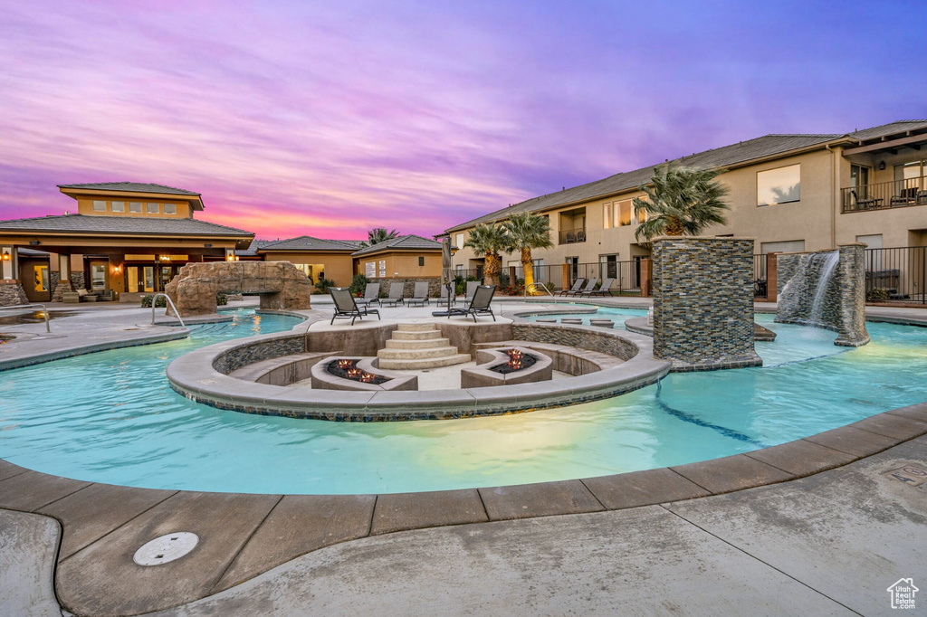 Pool at dusk featuring a hot tub, pool water feature, a patio, and an outdoor fire pit