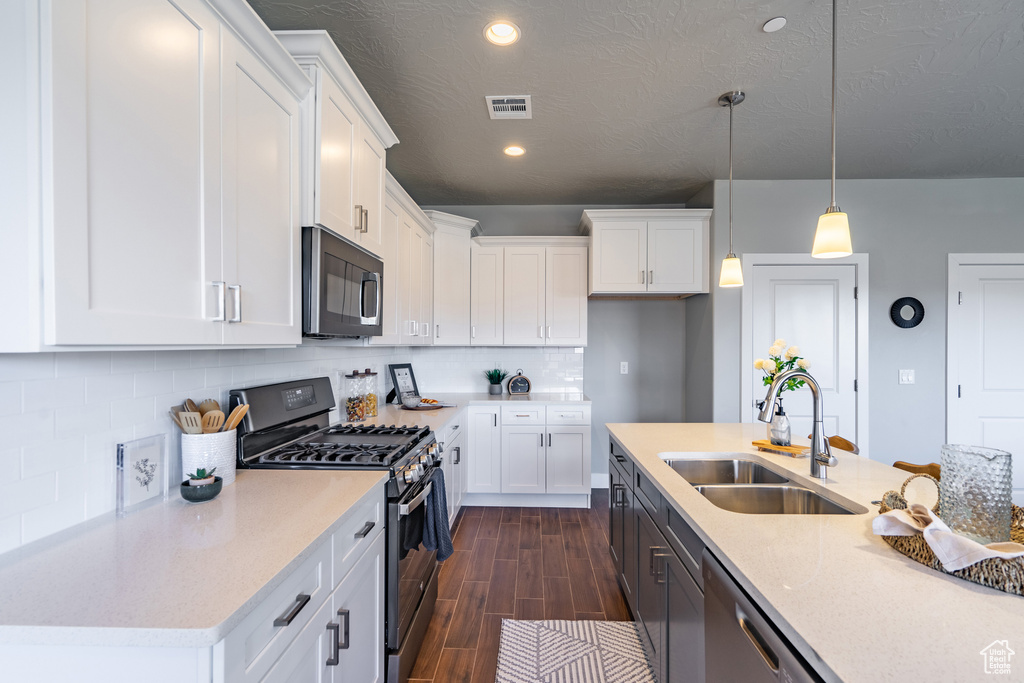 Kitchen featuring appliances with stainless steel finishes, hanging light fixtures, white cabinetry, a kitchen island with sink, and sink