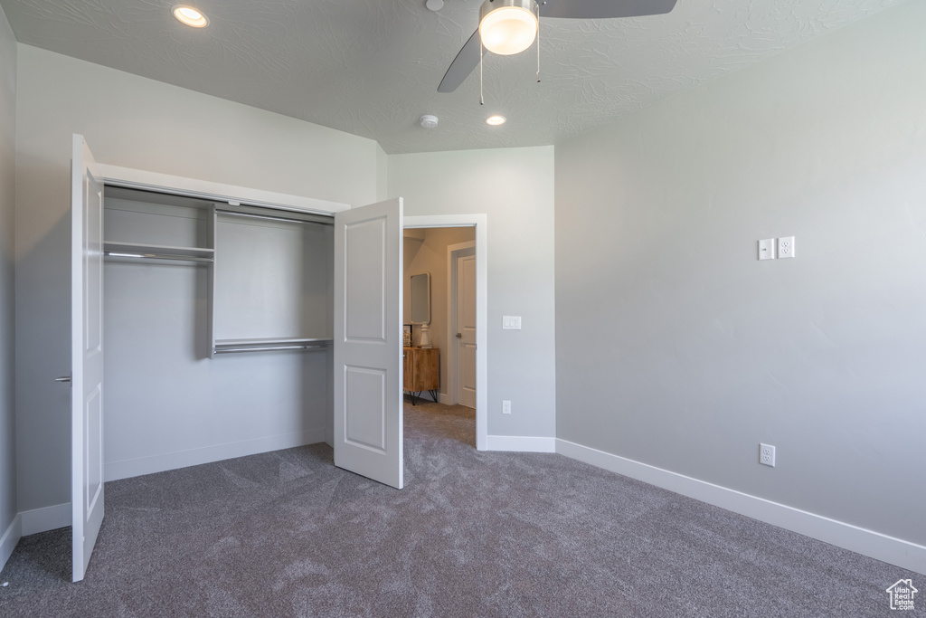 Unfurnished bedroom featuring dark colored carpet, a closet, ceiling fan, and a textured ceiling
