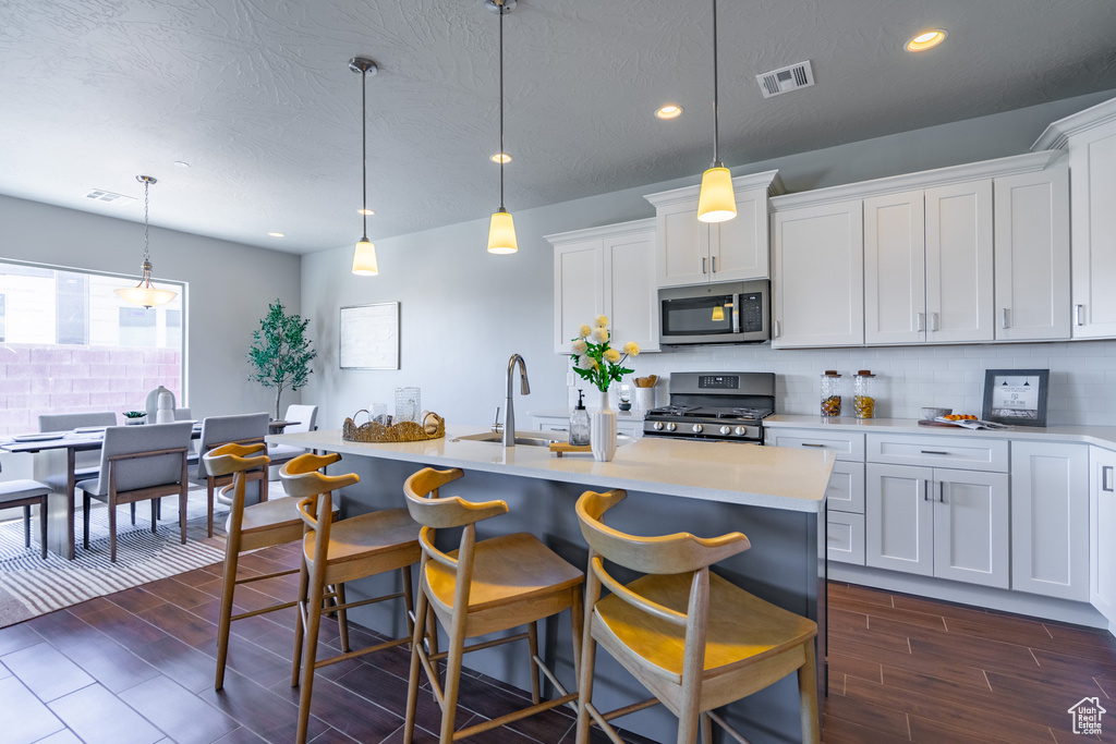 Kitchen with stainless steel appliances, white cabinets, dark hardwood / wood-style floors, and hanging light fixtures