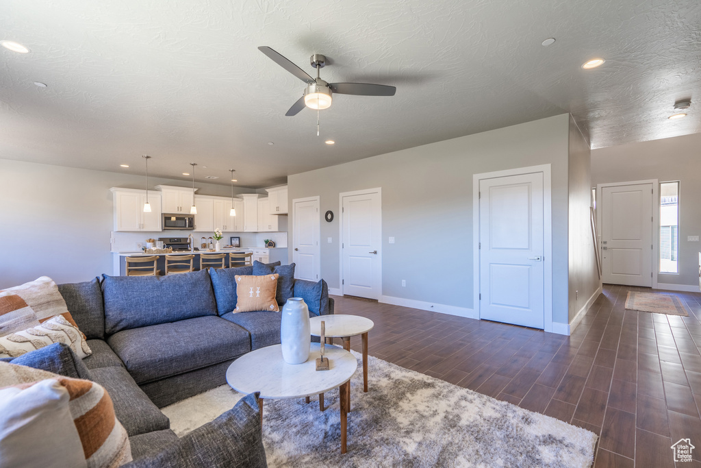 Living room with ceiling fan, a textured ceiling, and dark wood-type flooring