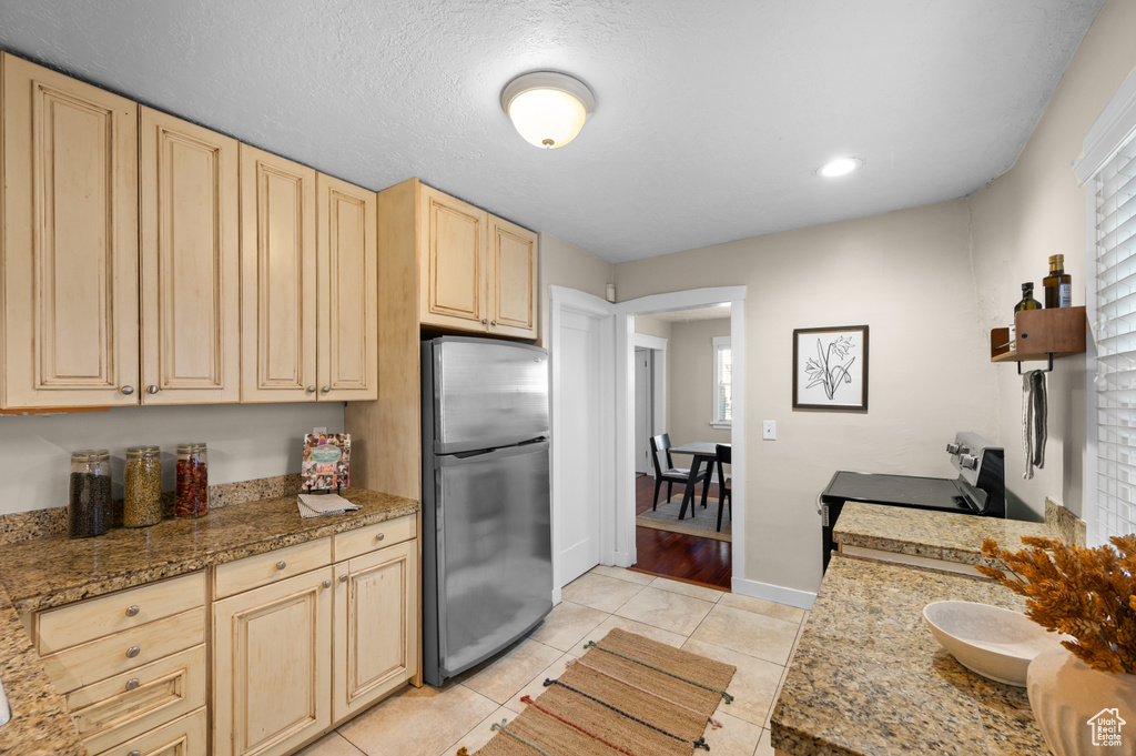 Kitchen featuring electric stove, stainless steel refrigerator, light brown cabinets, light tile patterned floors, and a textured ceiling