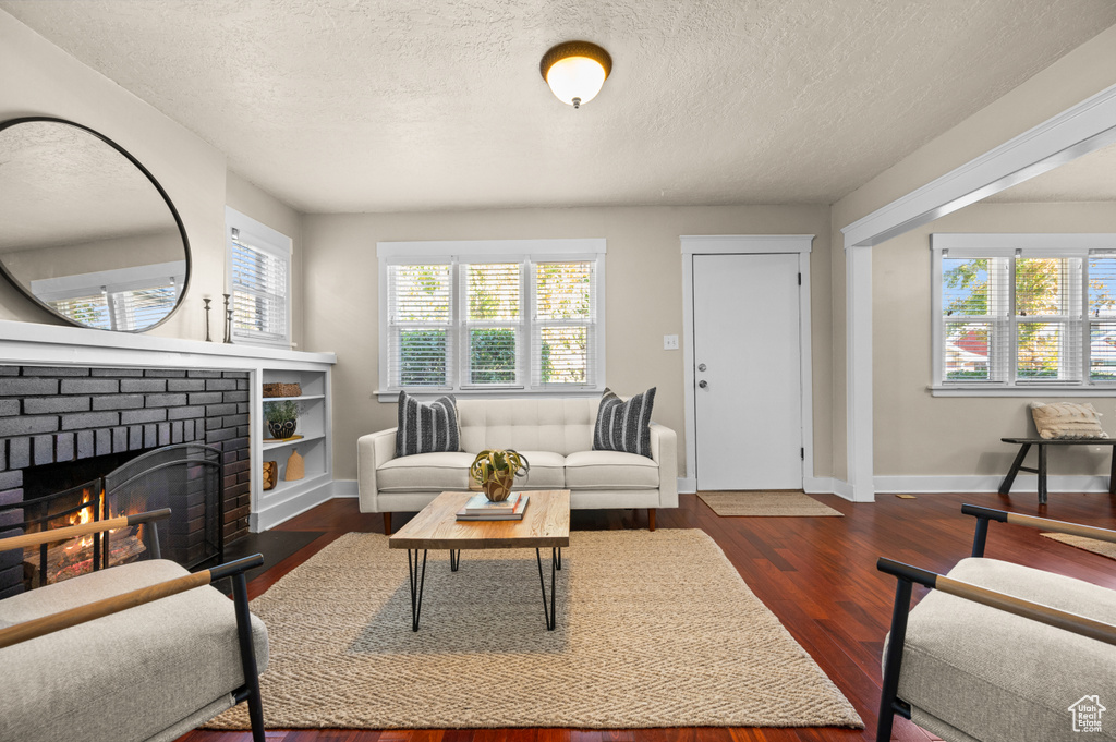 Living room featuring a brick fireplace, a textured ceiling, and dark wood-type flooring