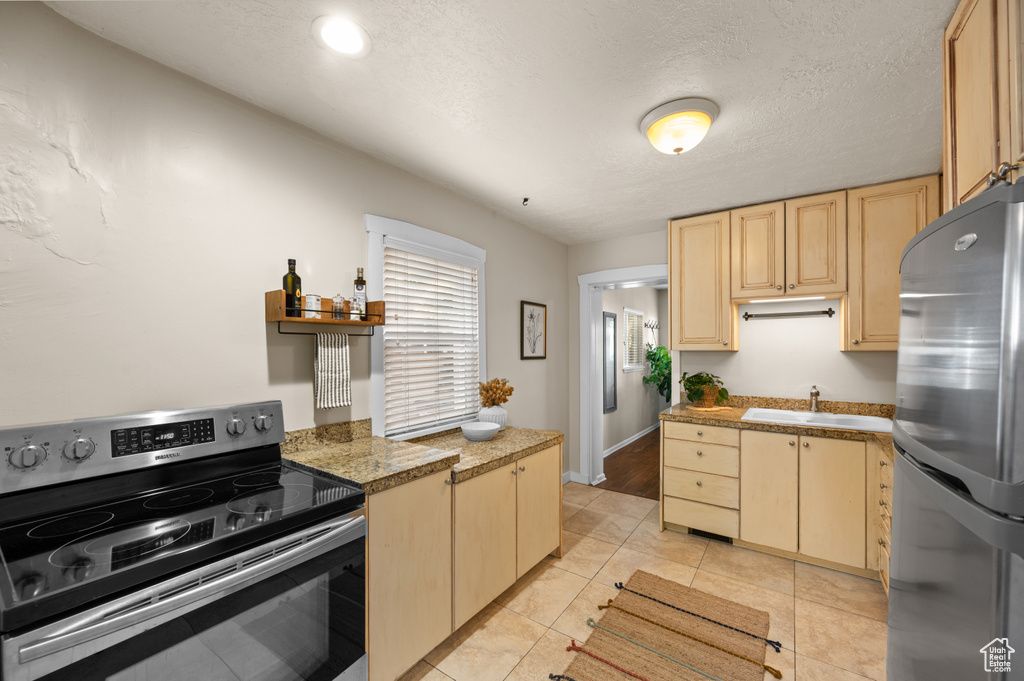 Kitchen with appliances with stainless steel finishes, light brown cabinetry, light tile patterned floors, and sink