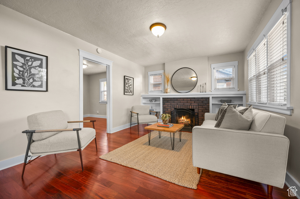 Living room with a healthy amount of sunlight, wood-type flooring, a textured ceiling, and a brick fireplace