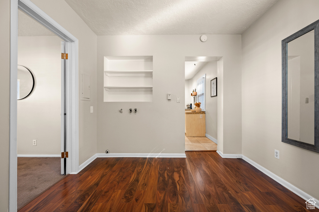 Laundry area featuring a textured ceiling, built in shelves, hookup for a washing machine, and dark wood-type flooring