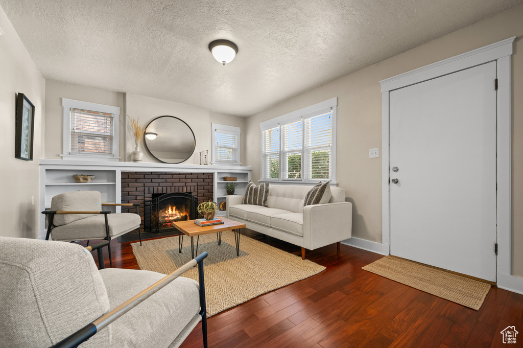 Living room with a brick fireplace, wood-type flooring, and a textured ceiling