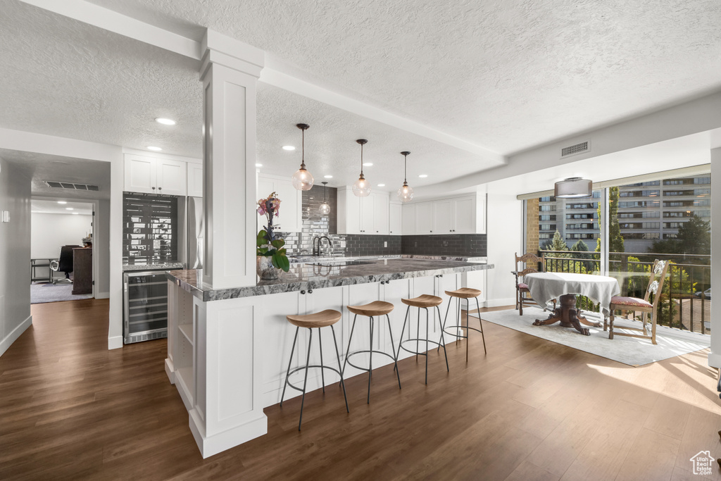 Kitchen with decorative backsplash, beverage cooler, white cabinetry, and dark hardwood / wood-style floors