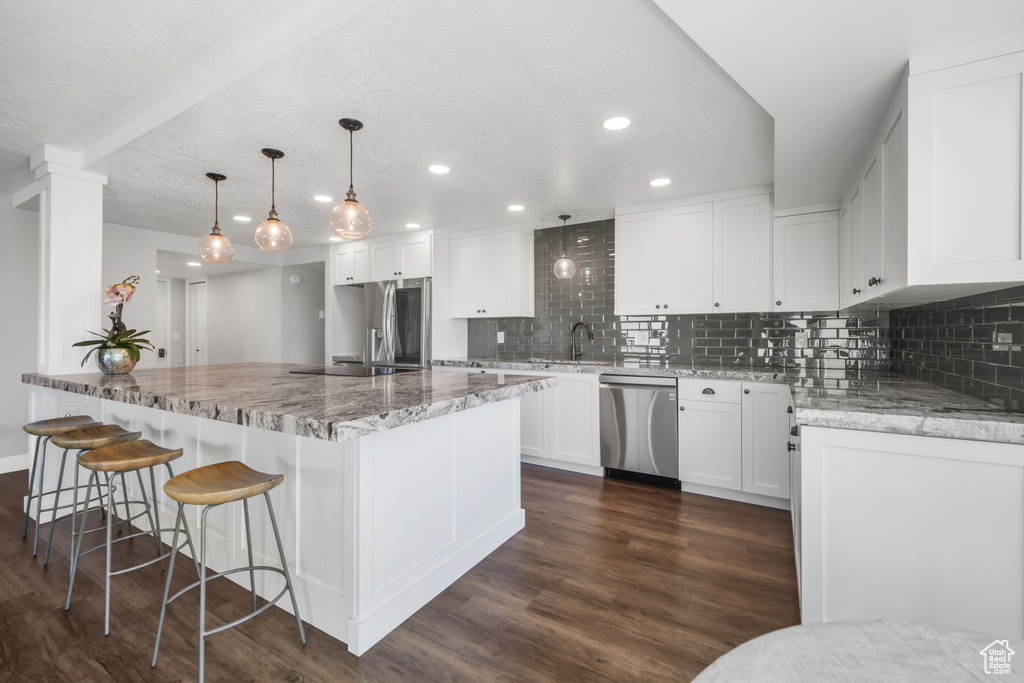 Kitchen featuring hanging light fixtures, white cabinetry, stainless steel appliances, dark hardwood / wood-style floors, and decorative backsplash