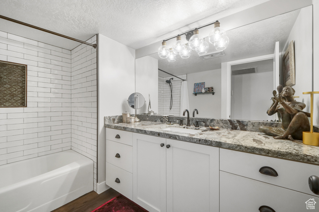 Bathroom featuring a textured ceiling, tiled shower / bath, hardwood / wood-style flooring, and vanity