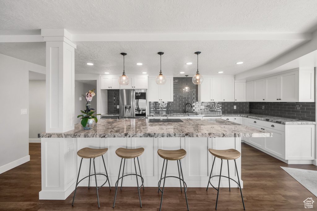 Kitchen featuring decorative light fixtures, backsplash, stainless steel fridge with ice dispenser, white cabinetry, and dark hardwood / wood-style flooring