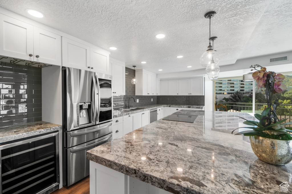 Kitchen with decorative backsplash, beverage cooler, stainless steel fridge with ice dispenser, and white cabinets