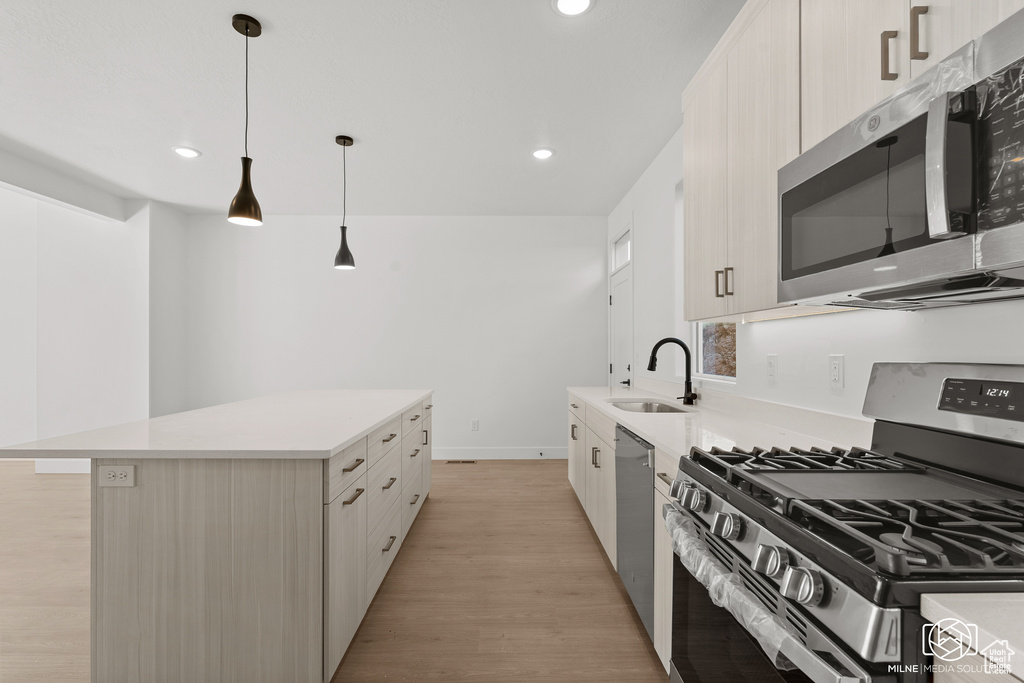 Kitchen with sink, decorative light fixtures, light hardwood / wood-style flooring, appliances with stainless steel finishes, and a center island