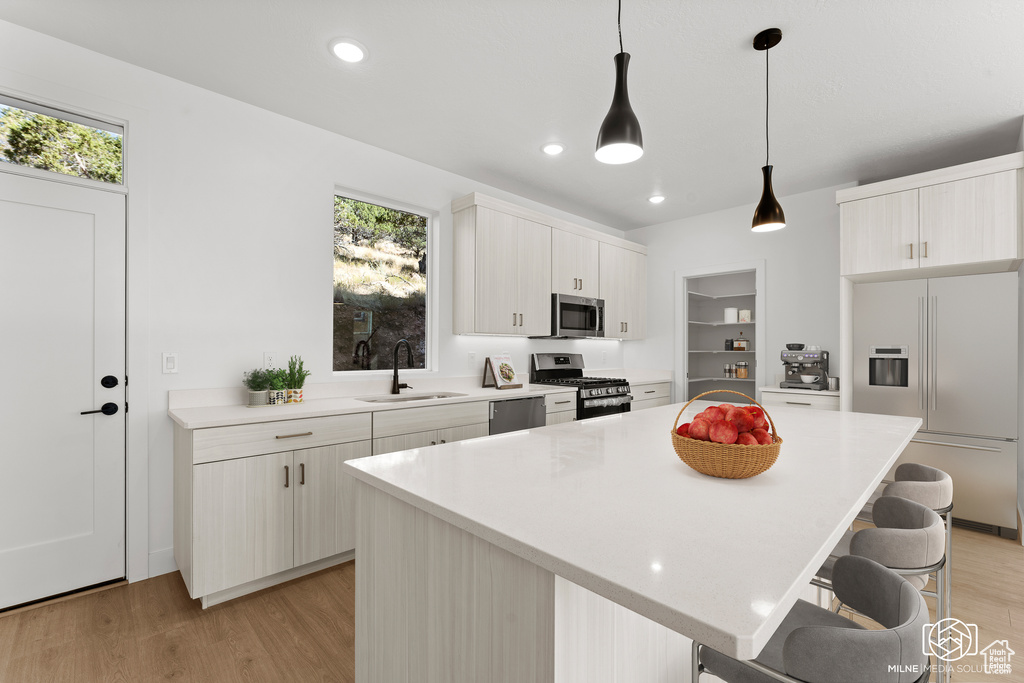 Kitchen with hanging light fixtures, light hardwood / wood-style floors, a kitchen island, stainless steel appliances, and sink