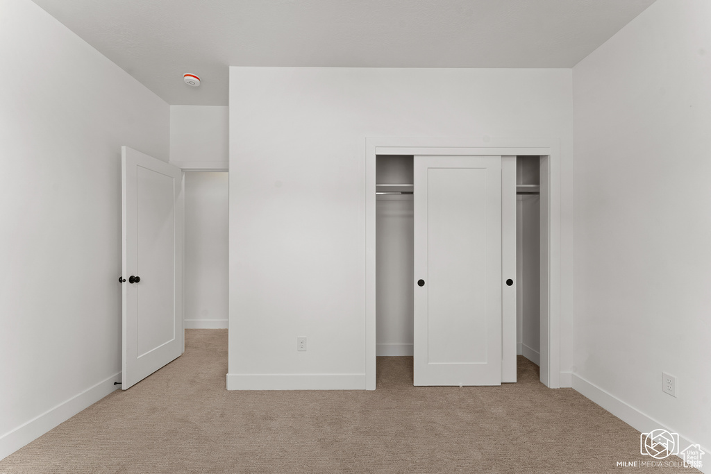 Unfurnished bedroom featuring light carpet and a closet