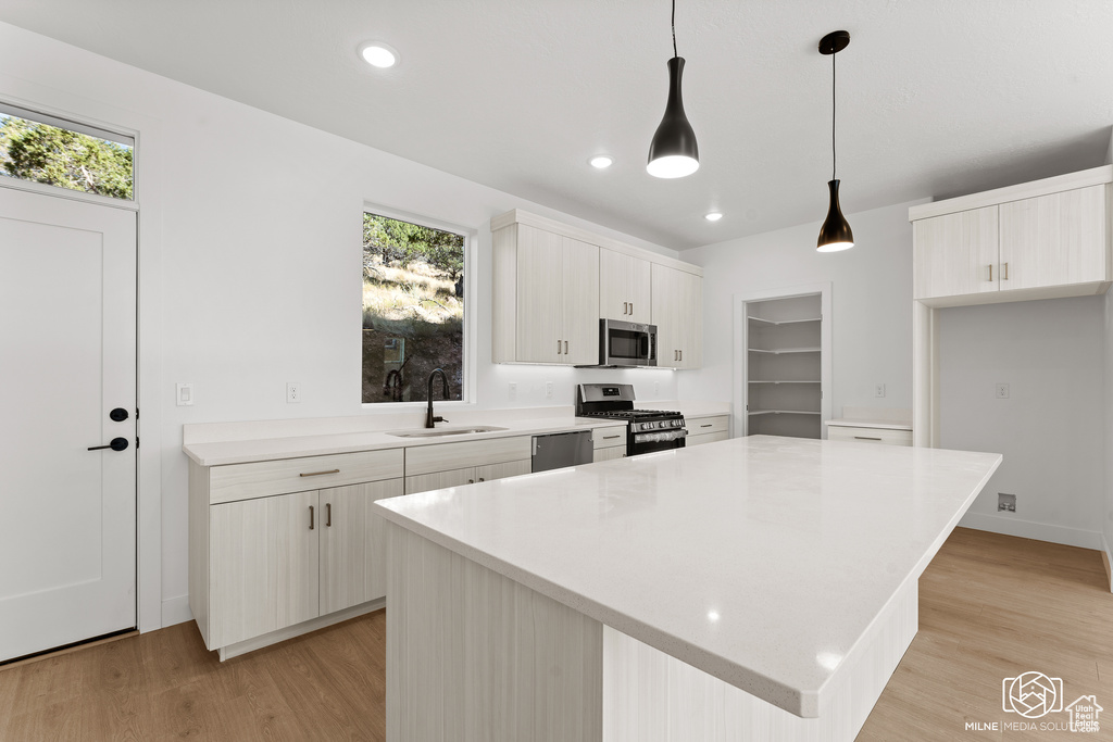 Kitchen featuring stainless steel appliances, light wood-type flooring, a center island, decorative light fixtures, and sink