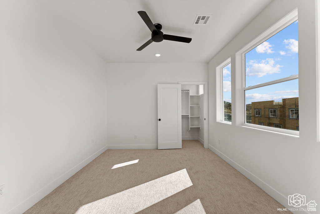 Unfurnished bedroom featuring light carpet, a closet, ceiling fan, and a walk in closet