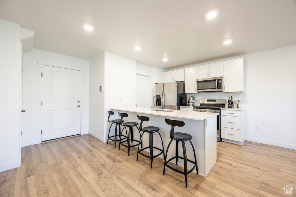 Kitchen with a breakfast bar, white cabinetry, kitchen peninsula, light hardwood / wood-style flooring, and stainless steel appliances