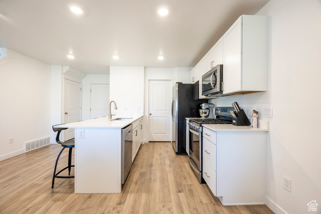 Kitchen featuring light hardwood / wood-style floors, sink, white cabinets, a kitchen bar, and appliances with stainless steel finishes