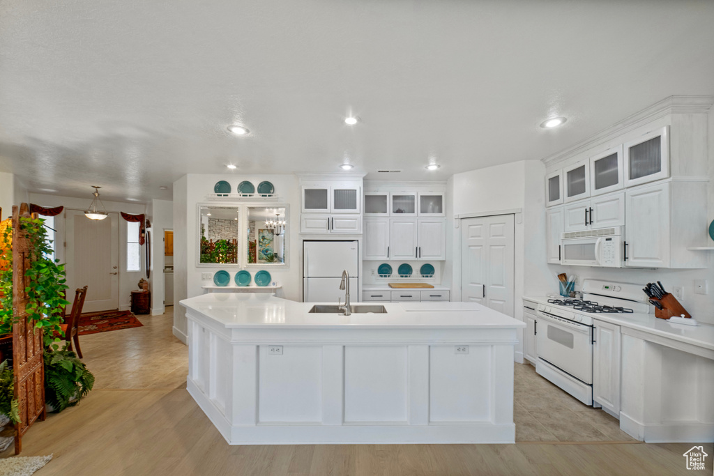 Kitchen featuring light hardwood / wood-style flooring, white appliances, an island with sink, and sink