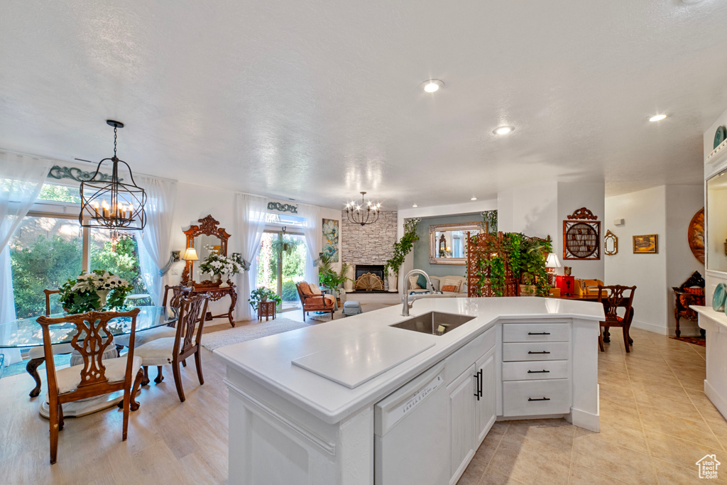 Kitchen with sink, an island with sink, white cabinetry, a fireplace, and white dishwasher