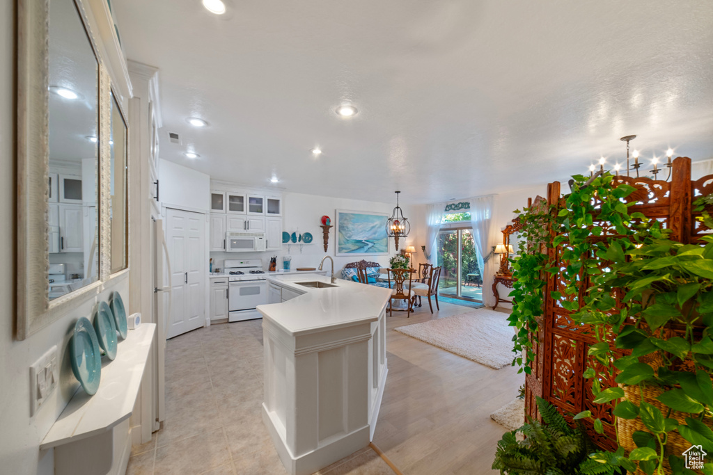 Kitchen featuring white cabinets, white appliances, decorative light fixtures, a kitchen island with sink, and a notable chandelier