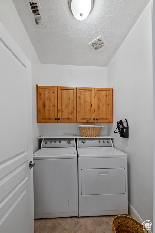 Washroom featuring cabinets, light tile patterned floors, washer and clothes dryer, and a textured ceiling