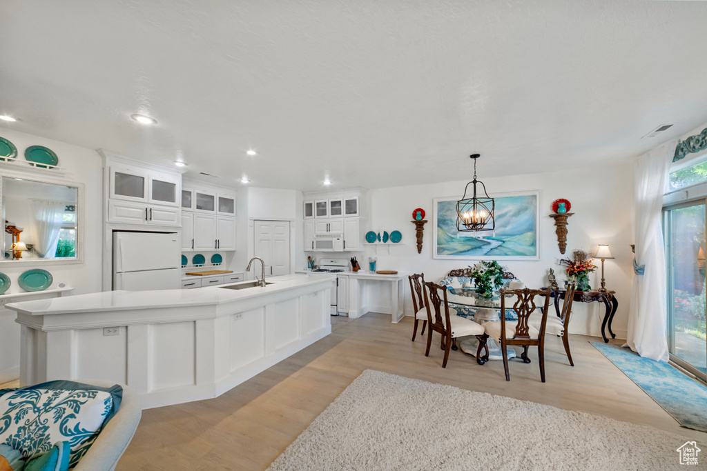 Kitchen featuring pendant lighting, sink, white cabinets, light hardwood / wood-style flooring, and white appliances