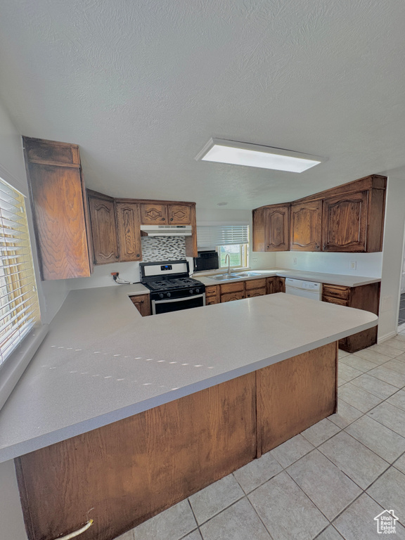 Kitchen featuring plenty of natural light, kitchen peninsula, stainless steel range with gas stovetop, and light tile patterned floors