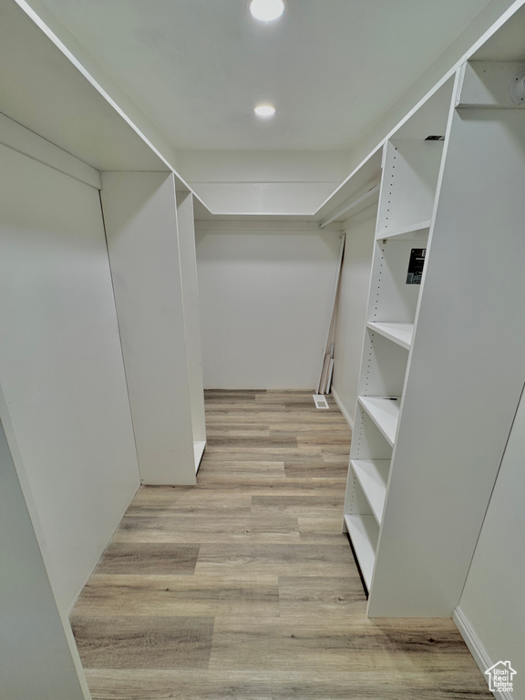 Walk in closet with light hardwood / wood-style flooring