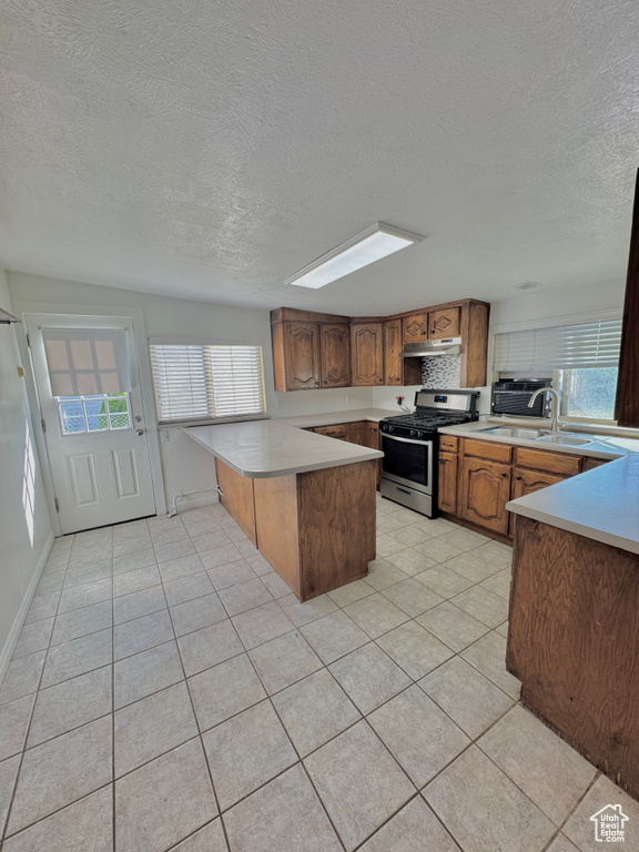 Kitchen with kitchen peninsula, stainless steel gas range oven, light tile patterned floors, and sink