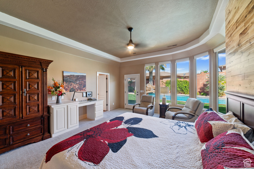 Carpeted bedroom featuring ceiling fan, a raised ceiling, access to exterior, and a textured ceiling