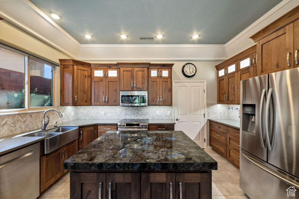 Kitchen with dark stone countertops, tasteful backsplash, stainless steel appliances, a center island, and sink