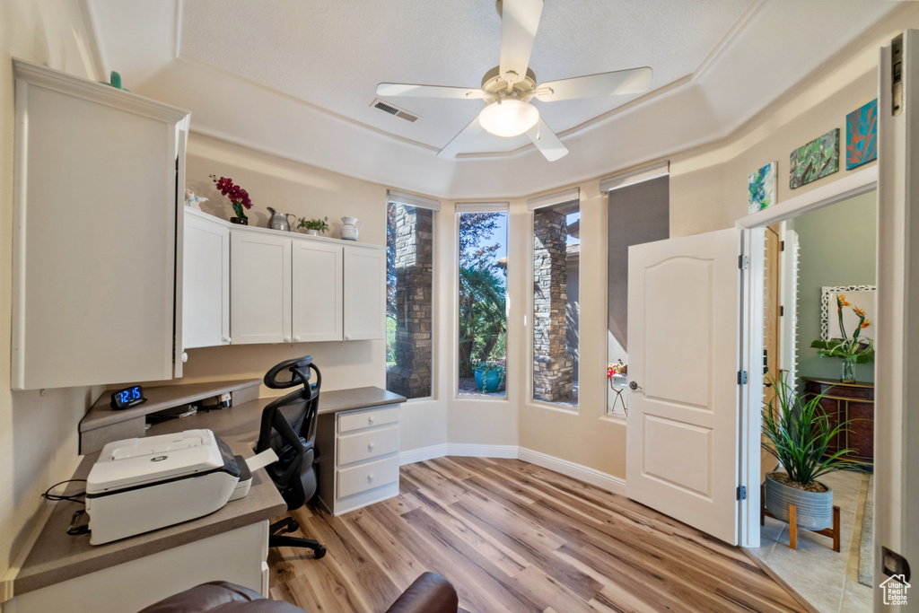 Office area with light hardwood / wood-style flooring, built in desk, ceiling fan, and a raised ceiling