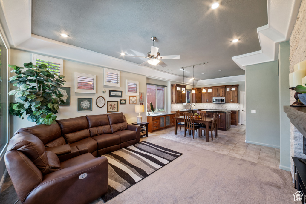 Living room with a raised ceiling, ceiling fan, light colored carpet, and a fireplace