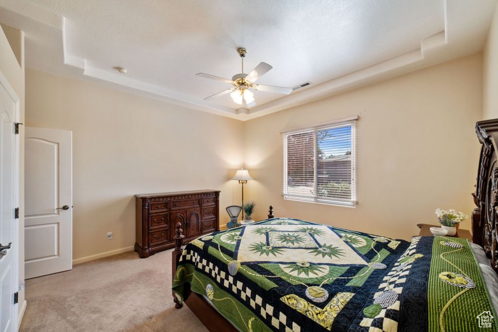 Bedroom with a tray ceiling, ceiling fan, and light colored carpet