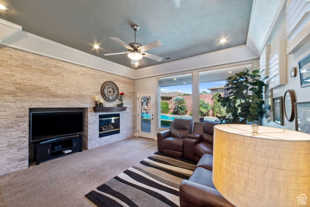 Living room with a textured ceiling, a stone fireplace, light carpet, and ceiling fan