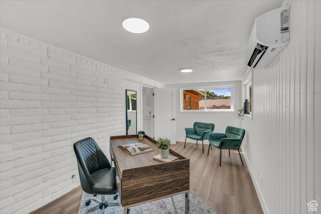 Office space with an AC wall unit, light hardwood / wood-style floors, and brick wall