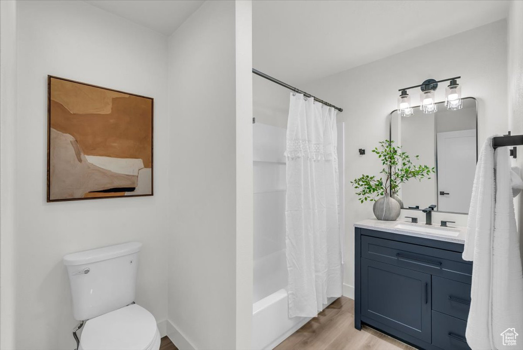 Full bathroom featuring shower / bathtub combination with curtain, hardwood / wood-style floors, vanity, and toilet