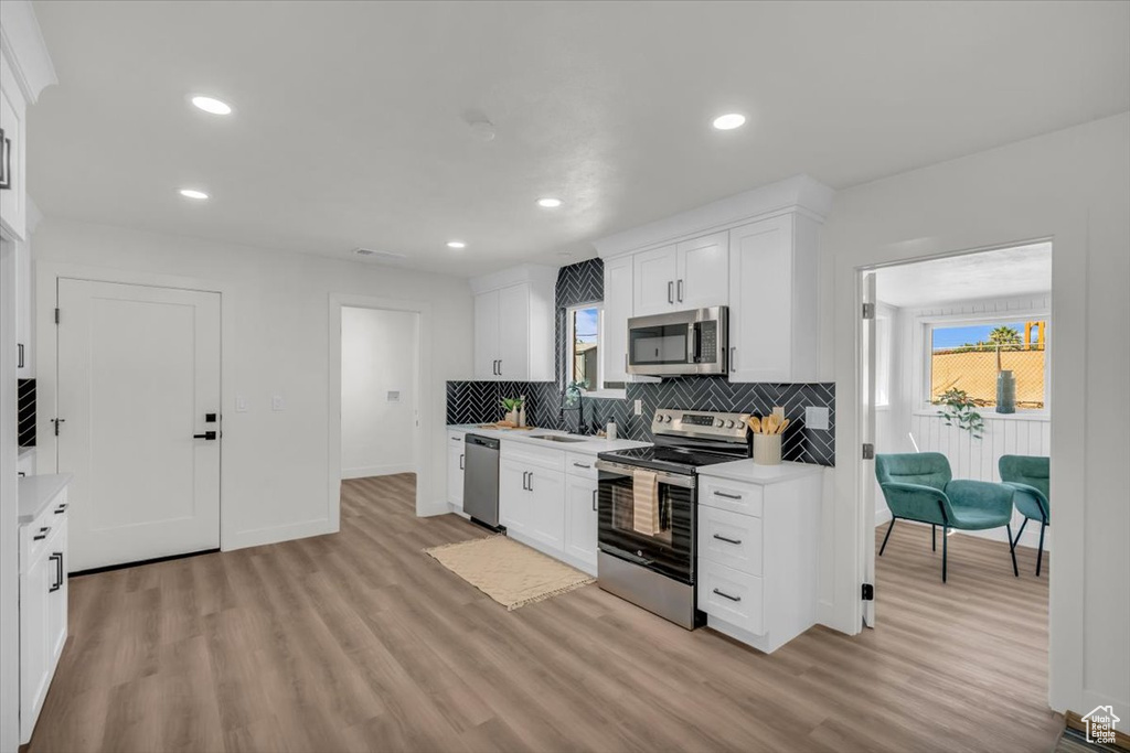 Kitchen with light hardwood / wood-style floors, sink, white cabinetry, decorative backsplash, and stainless steel appliances