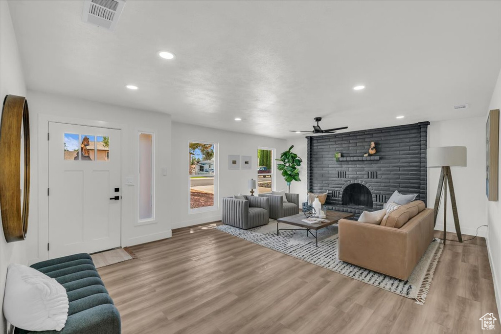 Living room featuring a brick fireplace, light wood-type flooring, and ceiling fan