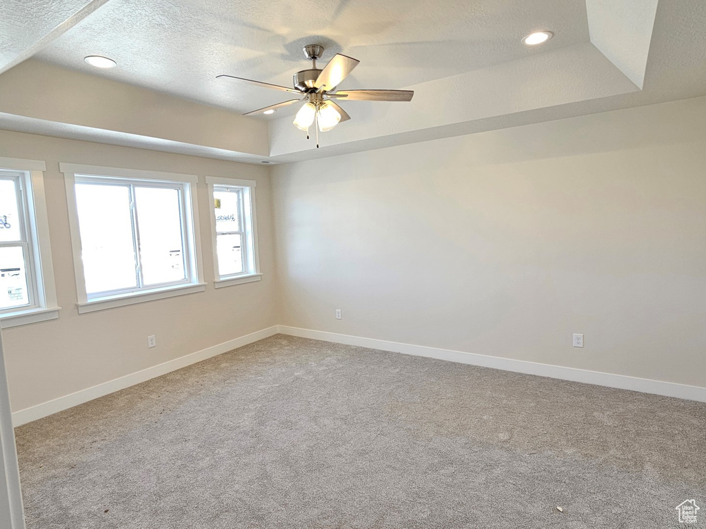 Empty room featuring a textured ceiling, a raised ceiling, ceiling fan, and light colored carpet