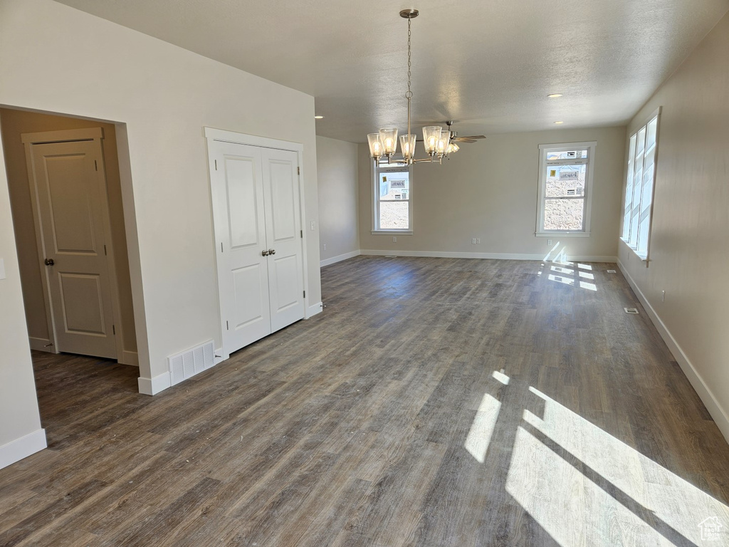 Unfurnished dining area with a textured ceiling, ceiling fan with notable chandelier, and dark wood-type flooring