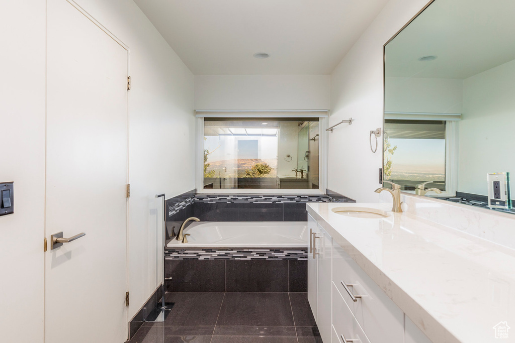 Bathroom with a relaxing tiled tub, tile patterned flooring, and vanity