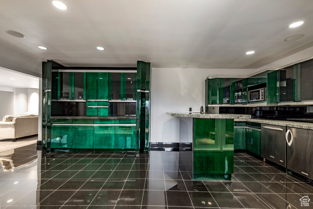 Kitchen featuring dark tile patterned flooring, light stone countertops, appliances with stainless steel finishes, and green cabinets