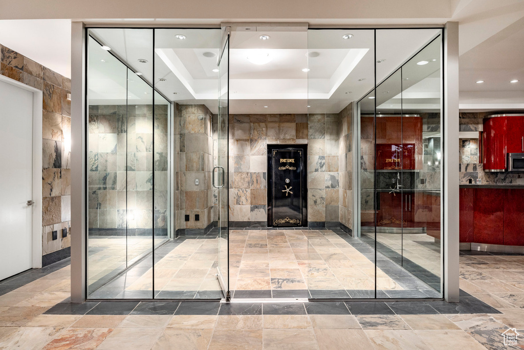 Bathroom with a tray ceiling, a shower with door, and tile walls